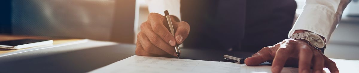 Nahaufnahme einer Hand, die mit einem Stift auf einem Papier unterschreibt.