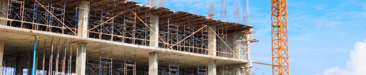 Baustelle mit Rohbau eines mehrstöckigen Gebäudes und gelbem Baukran vor blauem Himmel.