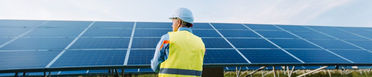 Ingenieur mit Schutzhelm und Warnweste vor einer großen Photovoltaikanlage, Symbol für Betreiberhaftpflichtversicherung im Bereich erneuerbare Energien.