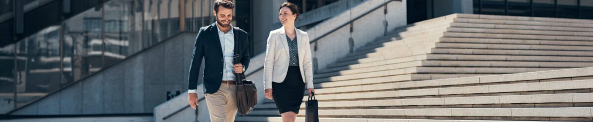 Geschäftsmann und Geschäftsfrau gehen vor einem Bürogebäude – Symbolbild für Haftpflichtversicherung und Unternehmensservices.