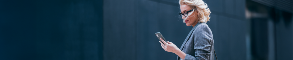Geschäftsfrau im Anzug schaut auf ihr Smartphone im Außenbereich – Symbolbild für Manager-Strafrechtsschutz und persönliche Haftungsrisiken.
