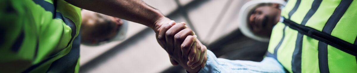 Zwei Bauarbeiter in Schutzwesten und Helmen geben sich die Hand – Symbolbild für Vertrauen und Absicherung durch Montageversicherung.