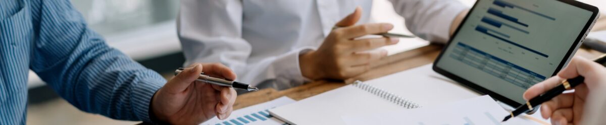 Geschäftsleute analysieren Finanzdiagramme und Statistiken auf Papier und Tablet, Symbol für Prospektprüfung und Absicherung von Kapitalmaßnahmen.