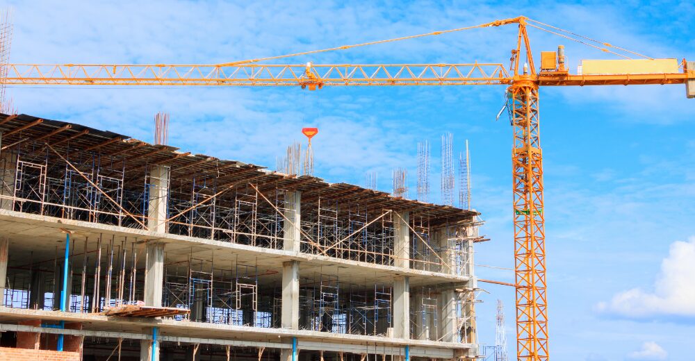 Baustelle mit Rohbau eines mehrstöckigen Gebäudes und gelbem Baukran vor blauem Himmel.