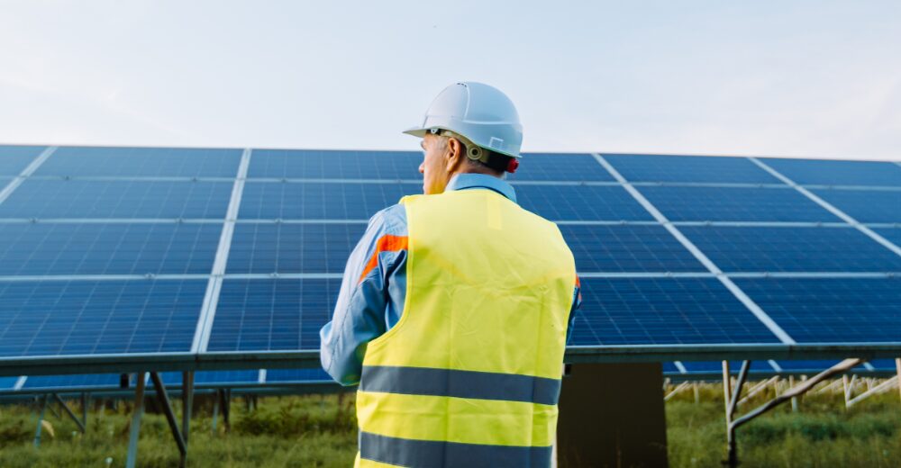 Ingenieur mit Schutzhelm und Warnweste vor einer großen Photovoltaikanlage, Symbol für Betreiberhaftpflichtversicherung im Bereich erneuerbare Energien.