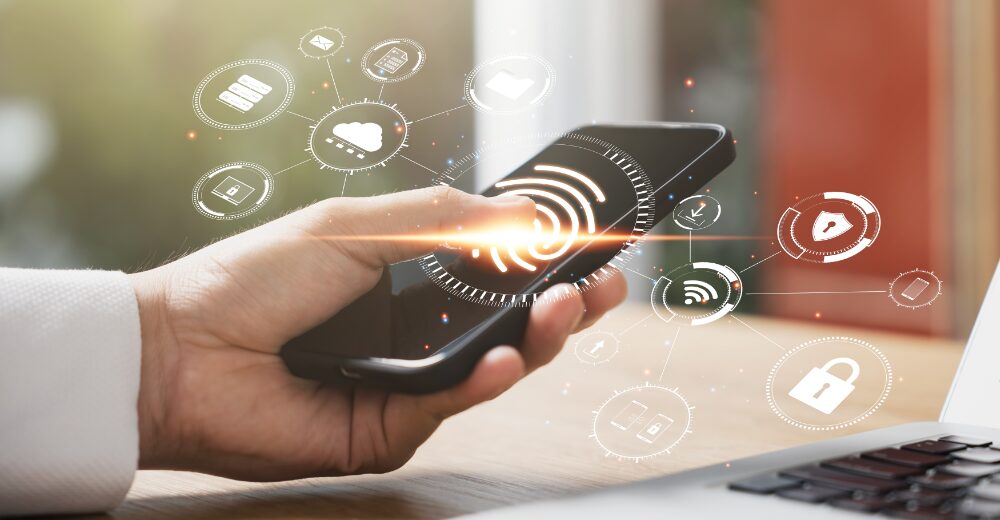 Hand hält Smartphone mit digital eingeblendeten Symbolen zu Cloud, WLAN und Sicherheit – Darstellung von Cybercrime und IT-Sicherheit.