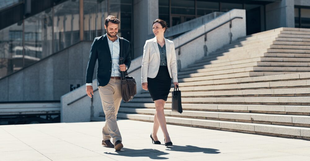 A businessman and a businesswoman walking in front of an office building – a symbolic image representing liability insurance and corporate services.