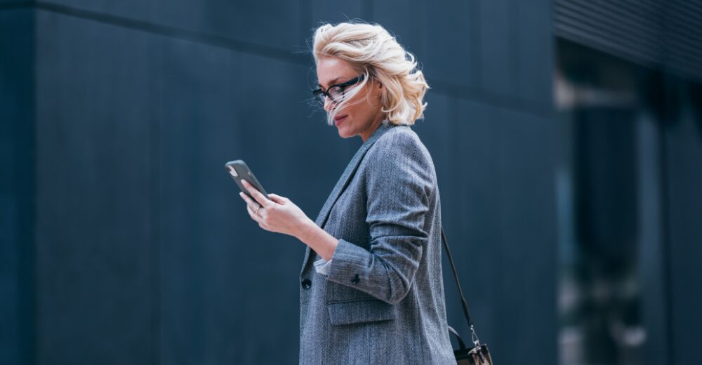 Geschäftsfrau im Anzug schaut auf ihr Smartphone im Außenbereich – Symbolbild für Manager-Strafrechtsschutz und persönliche Haftungsrisiken.