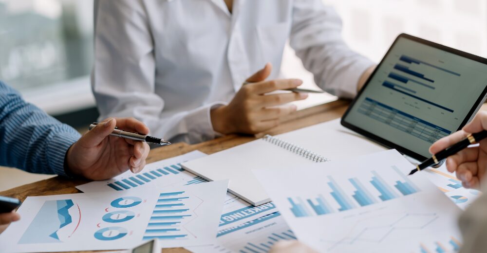 Geschäftsleute analysieren Finanzdiagramme und Statistiken auf Papier und Tablet, Symbol für Prospektprüfung und Absicherung von Kapitalmaßnahmen.