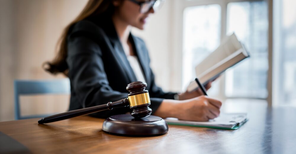 Frau schreibt in ein Notizbuch neben Richterhammer auf dem Schreibtisch – Symbolbild für Rechtsschutzversicherung für Selbstständige.