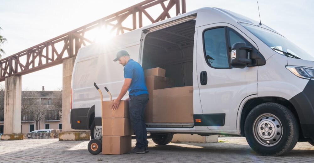 Lieferfahrer lädt Kartons mit einer Sackkarre aus einem Transporter – Symbolbild für Verkehrshaftungsversicherung und Speditionsrisiken.