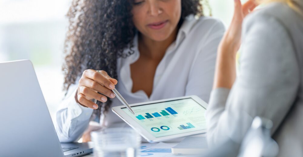 Beraterin erklärt einer Kundin Finanzdiagramme auf einem Tablet, Symbol für Beratung, Risikoanalyse und individuelle Versicherungslösungen.