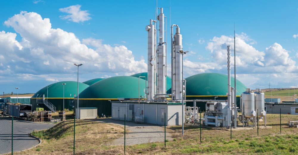 Biogasanlage mit grünen Kuppeln und technischer Industrieanlage im Vordergrund – Symbolbild für Versicherung von Biogasanlagen, Blockheizkraftwerken und Kraftwerken.