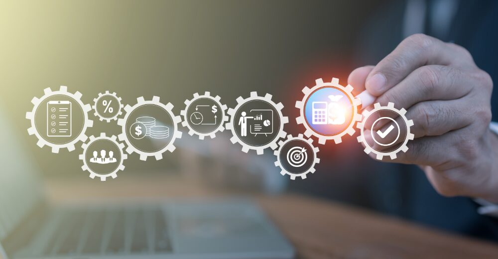 Geschäftsmann zeigt auf digitale Zahnräder mit Symbolen für Finanzen, Steuern, Kalkulation, Team und Strategie – Darstellung eines ganzheitlichen Management- und Versorgungskonzepts.