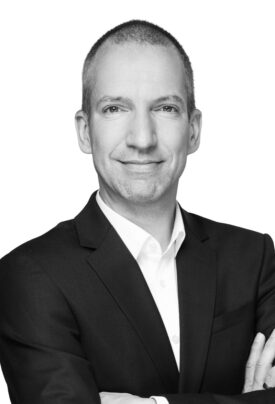Portrait of a smiling man in a suit with arms crossed, in front of a white background.