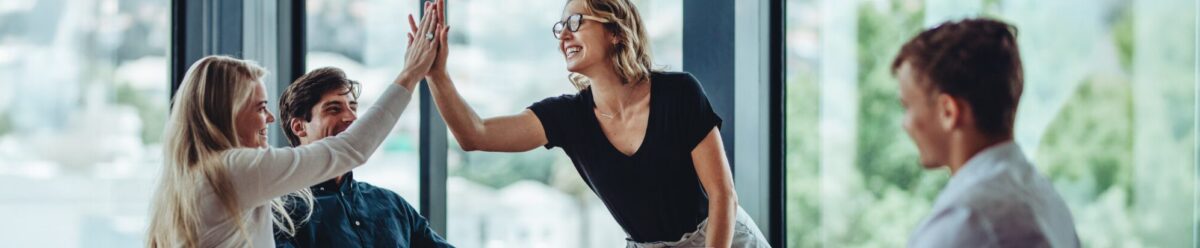 Vier Personen in einem modernen Büro, zwei davon geben sich lächelnd ein High Five in einer Teamsituation.