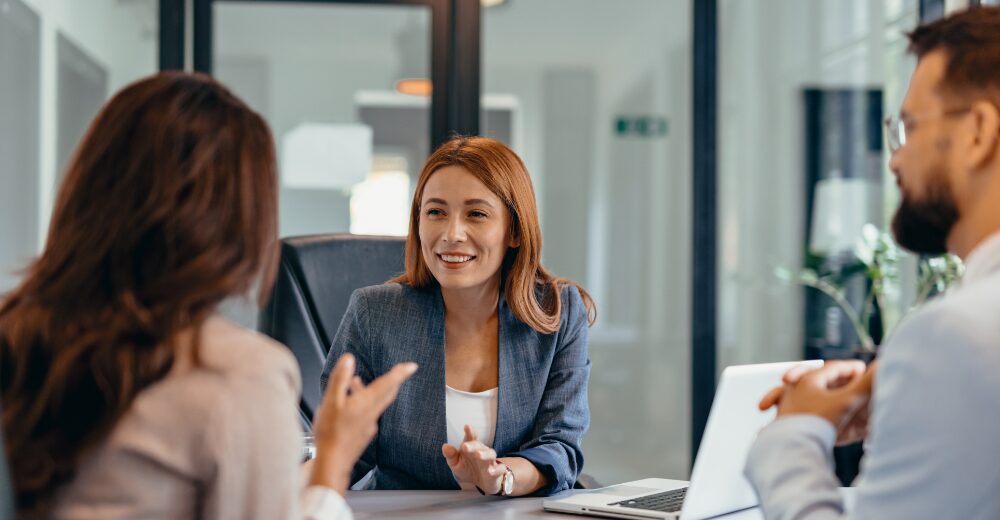 Person lächelt in einem Gespräch in einem modernen Büro, zwei weitere Personen sitzen gegenüber.