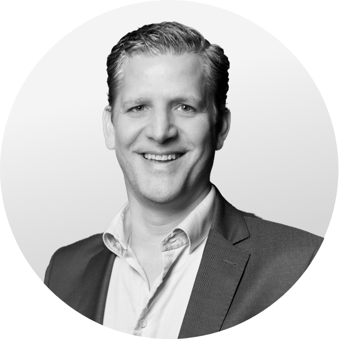 Porträt eines lächelnden Mannes im Anzug mit offenem Hemdkragen, vor hellem, rundem Hintergrund.