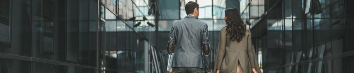 Geschäftsmann und Geschäftsfrau gehen gemeinsam durch ein modernes Bürogebäude mit Glaswänden.