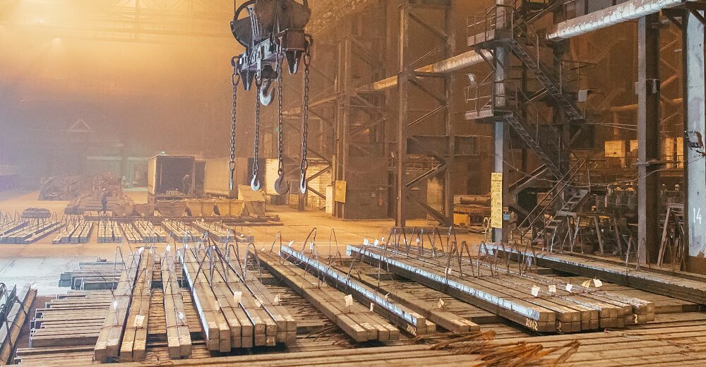 Große Industriehalle mit gelagerten Metallträgern und Produktionsanlagen im Hintergrund.