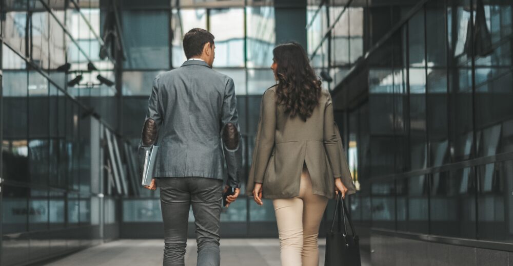 Geschäftsmann und Geschäftsfrau gehen gemeinsam durch ein modernes Bürogebäude mit Glaswänden.