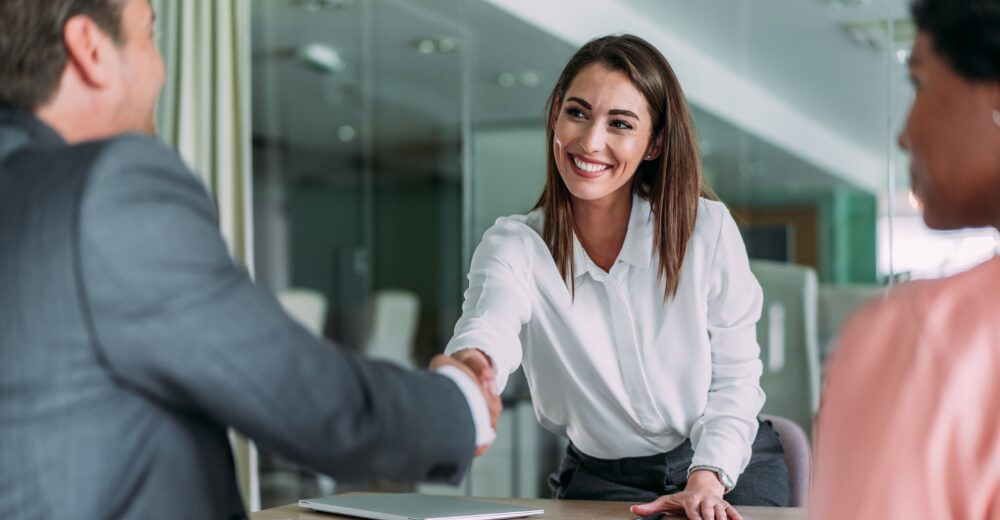 Geschäftsfrau schüttelt Kunden im Büro die Hand während eines Beratungsgesprächs zur Finanzkommunikation