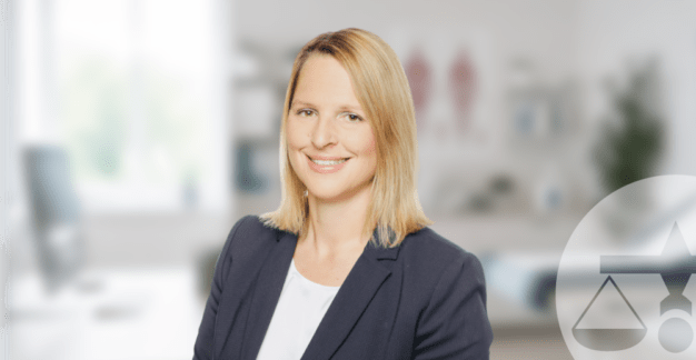 Sandra Mekler von MRH Trowe vor einem unscharfen Hintergrund einer Arztpraxis zum Thema betriebliche Gesundheitsversorgung und CancerSecure.