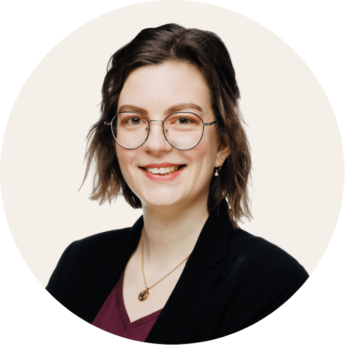 Porträtfoto von Katharina Krause. Sie trägt eine schwarze Jacke und eine Brille, hat schulterlange dunkle Haare und lächelt in die Kamera.
