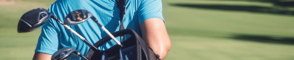 Ein Mann in einem blauen T-Shirt und einer schwarzen Kappe trägt einen Golfschläger-Rucksack auf einem Golfplatz.