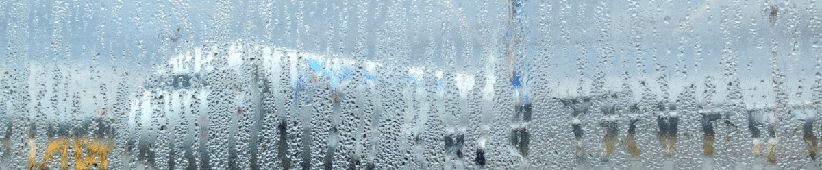 Blick durch eine beschlagene Scheibe auf einen Flughafen, wo Passagiere und Flughafenpersonal im Regen stehen.