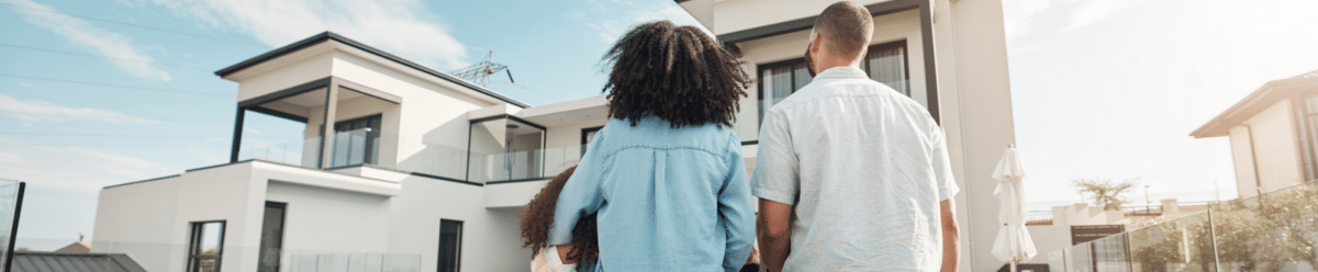 Familie mit zwei Kindern vor einem modernen Einfamilienhaus mit Garten.