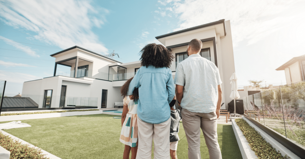 Familie mit zwei Kindern vor einem modernen Einfamilienhaus mit Garten.